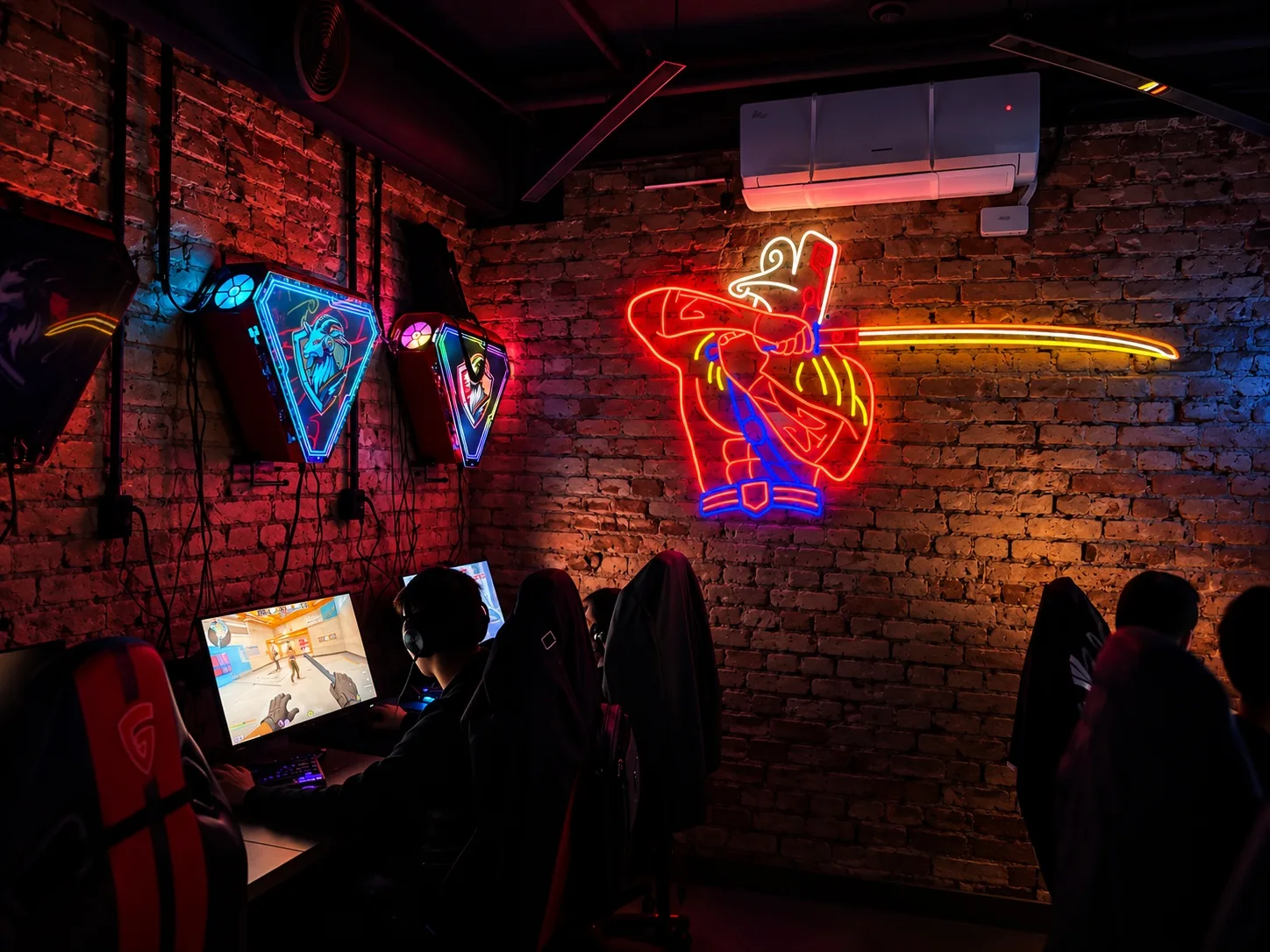 Зал Gonzo Gaming: неоновый самурай на кирпичной стене, игровые станции